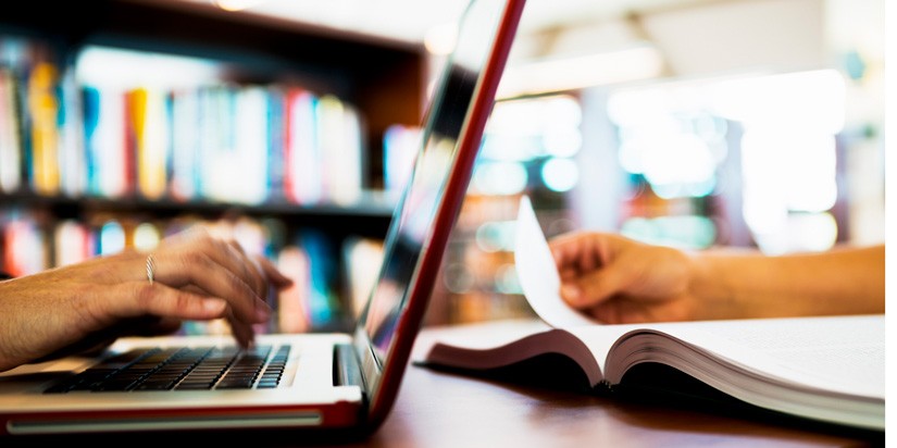 Photo of someone typing on a laptop and a someone turning the page of a book