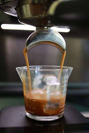 An espresso machine brews coffee into a glass measuring cup. 