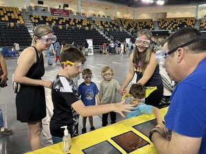 dults and children participating in a science experiment by holding hands next to a table inside a gym.